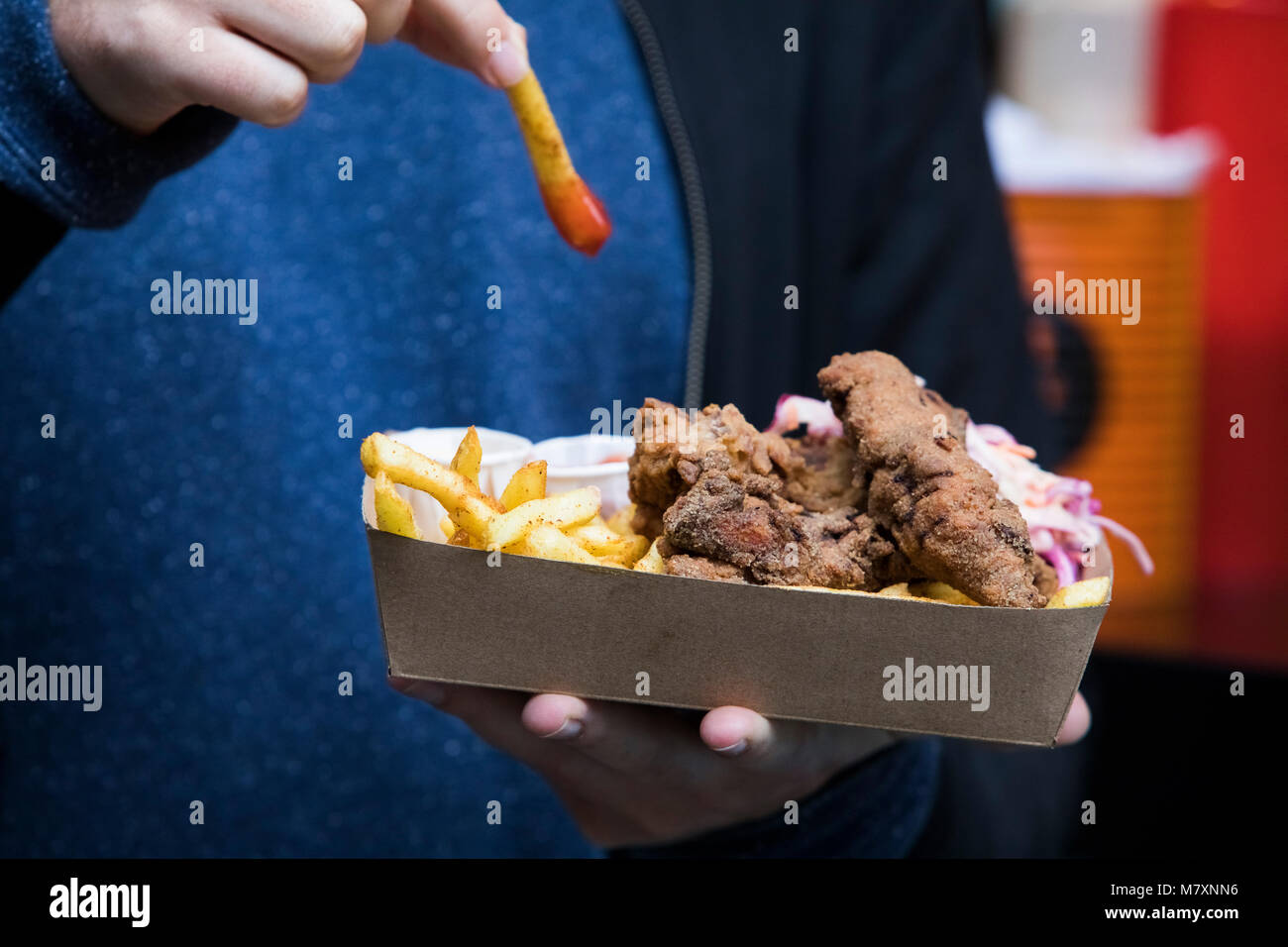 Man dipping chip in ketchup on takeaway tray. Stock Photo