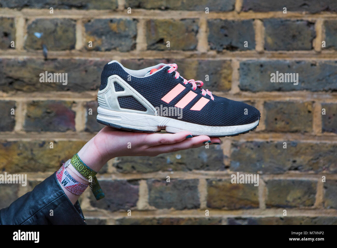 Cool vintage black Adidas trainer with pink stripes held by a woman. Stock Photo
