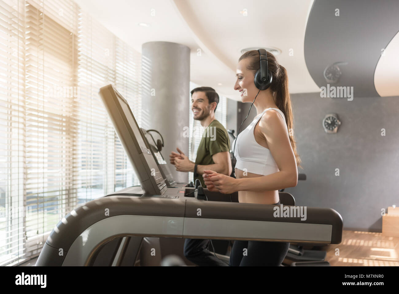 Young woman listening to music while running on a modern treadmill