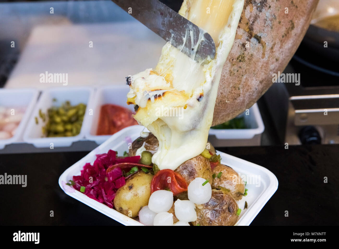 Raclette cheese on new potatoes with pickles. Stock Photo