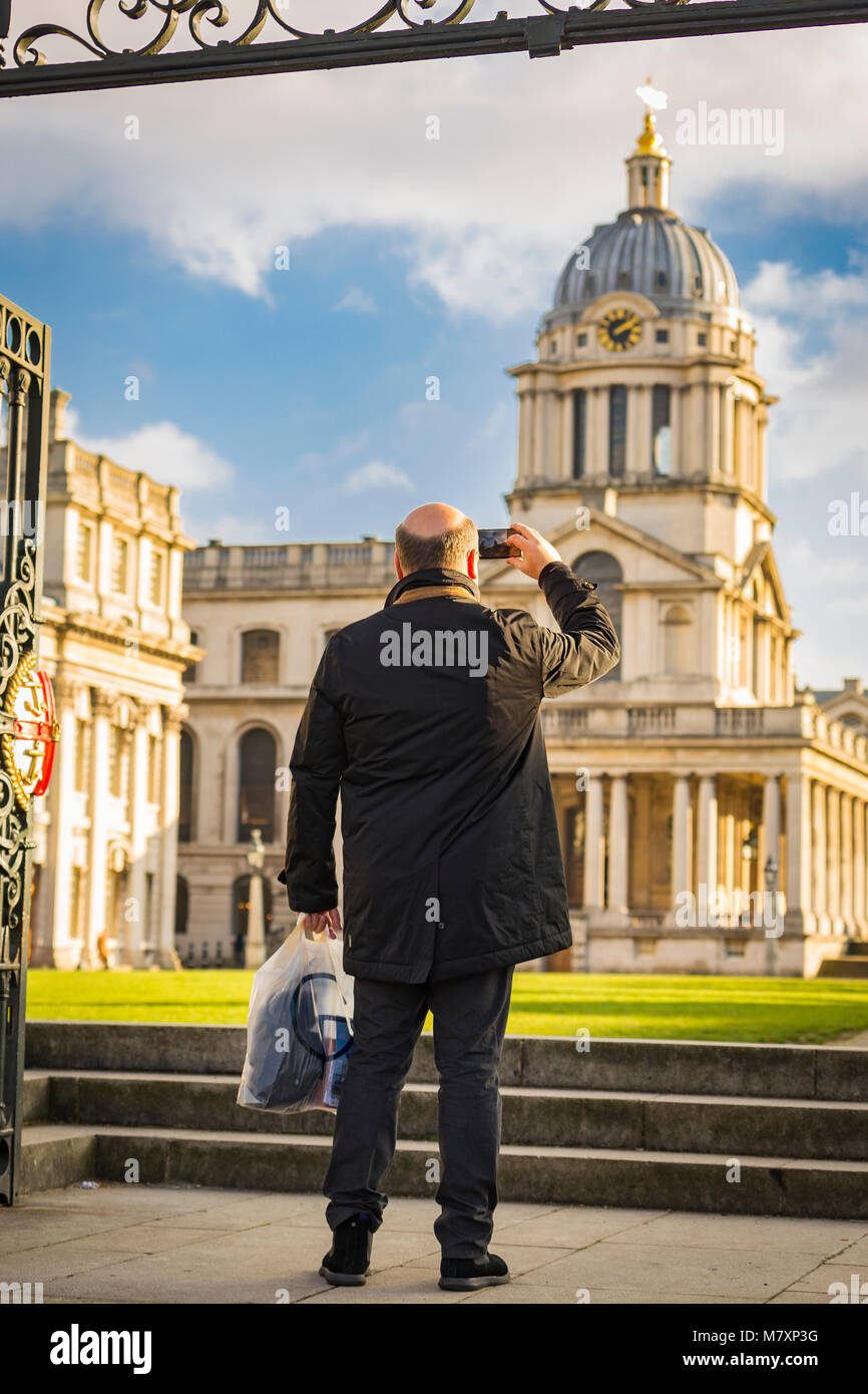 LONDON, UK - JAN 2018: Middle-aged male tourist taking photo of Royal Naval College in Greenwich on his cellphone Stock Photo