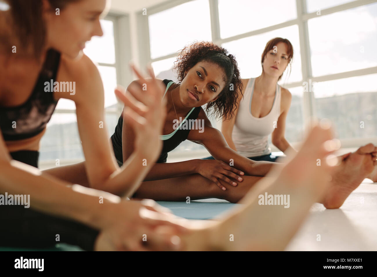 Young female relaxing and talking after workout session. Female friends during yoga class break at fitness center. Stock Photo