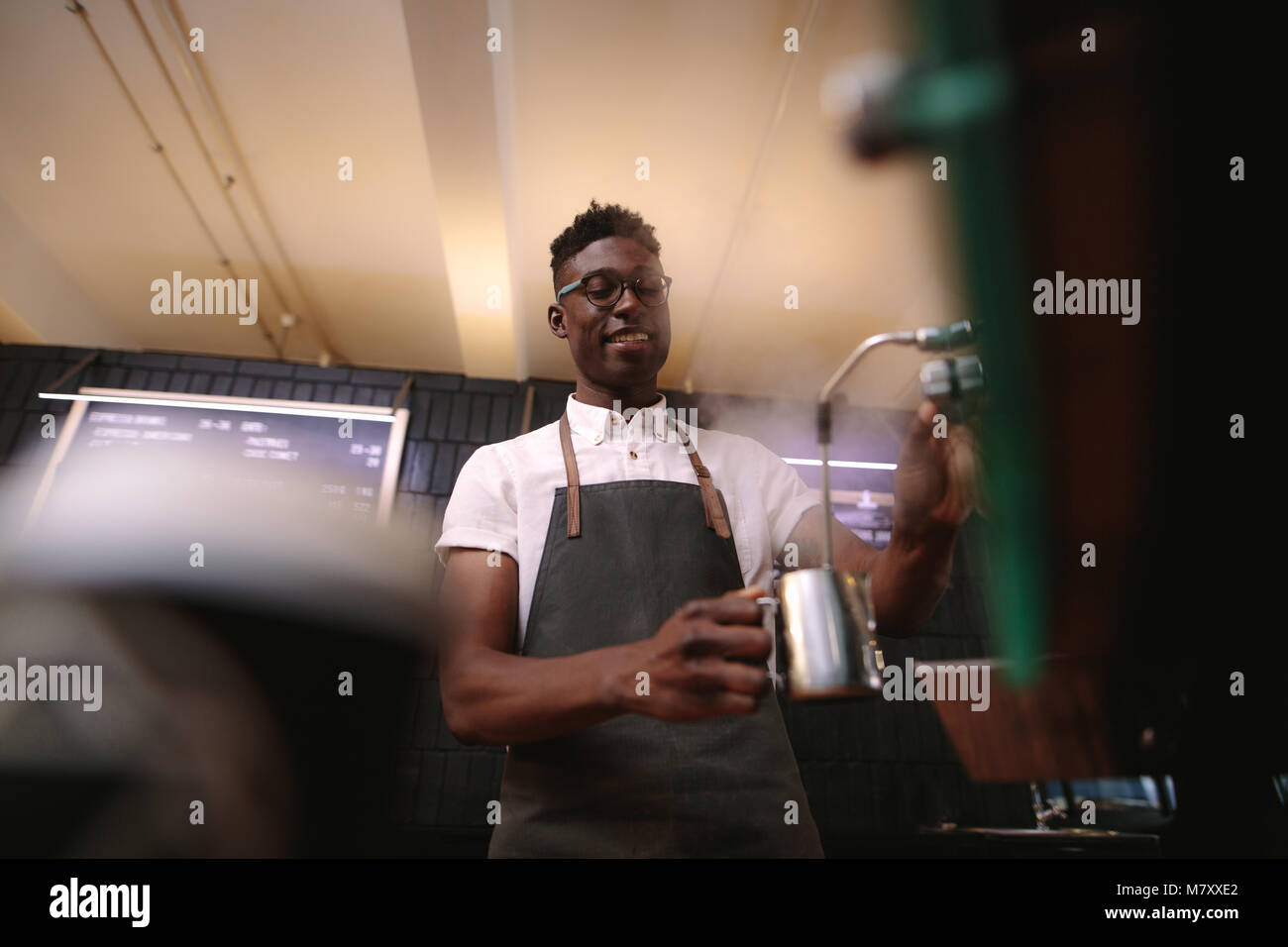 Coffee shop owner preparing coffee on steam espresso coffee machine. Man working in his coffee shop wearing an apron. Stock Photo