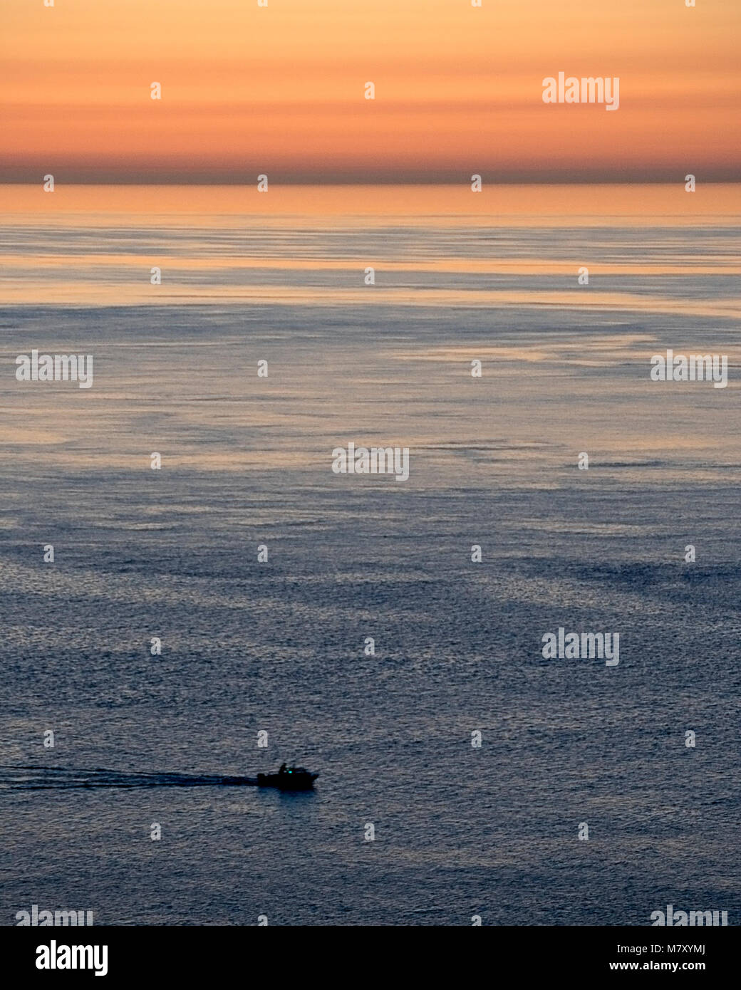 Solitary small boat on the sea at dusk off the coast of Anglesey, North Wales Stock Photo