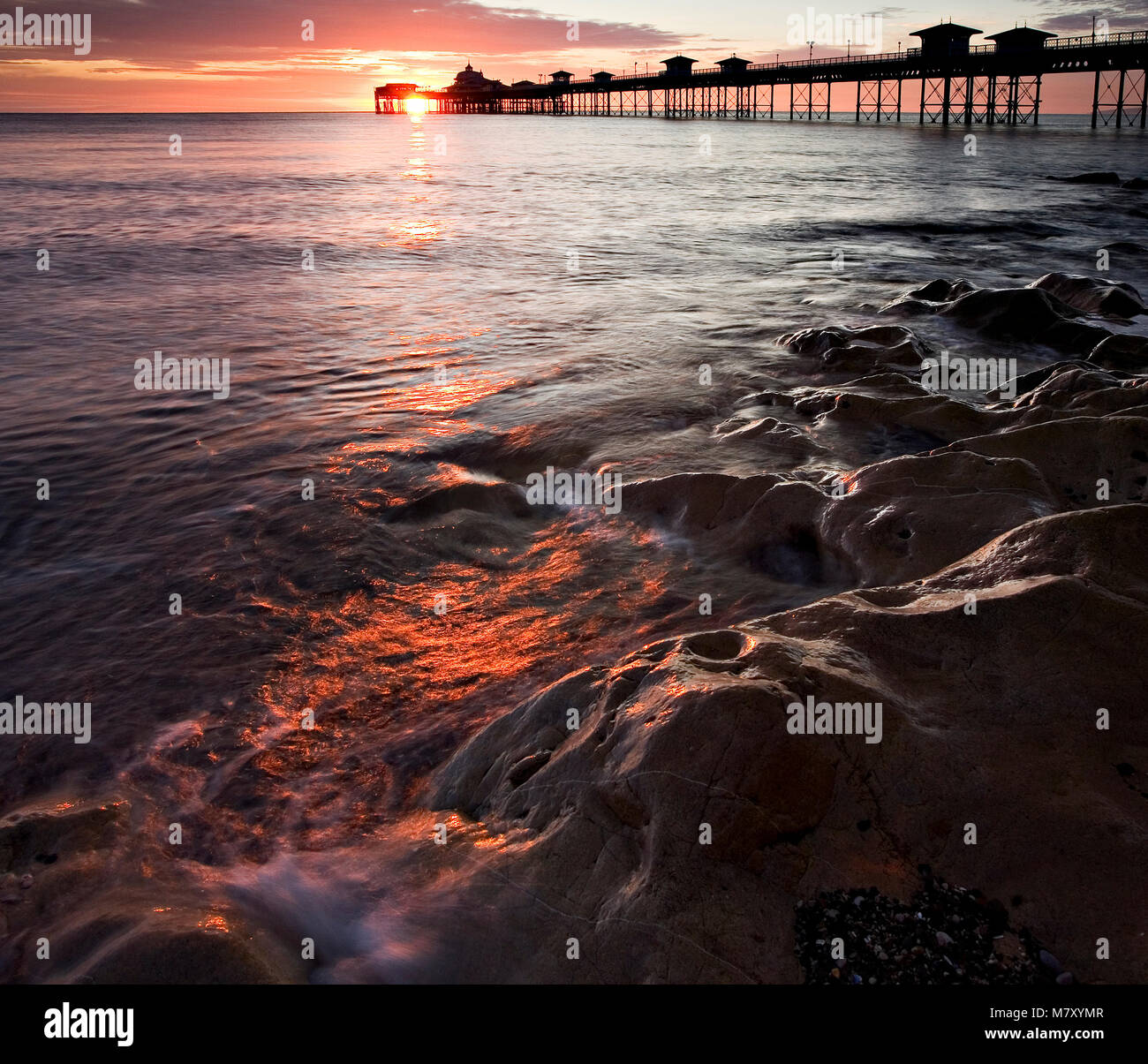 Llandudno pier at sunrise with waves on rocks on the North Wales coast Stock Photo