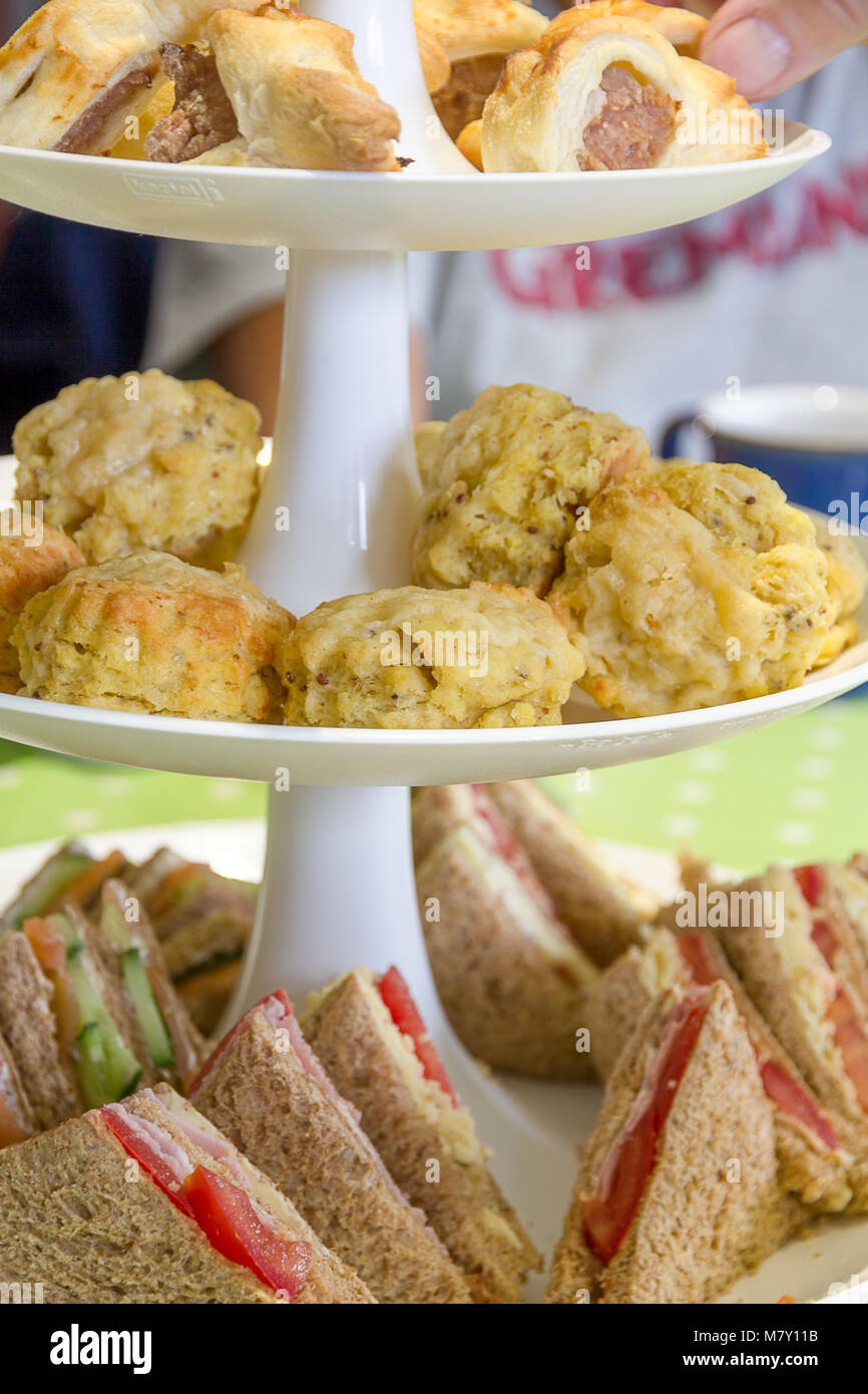 English afternoon tea consisting of sandwiches, cheese scones and sausage rolls on a tiered cake stand Stock Photo