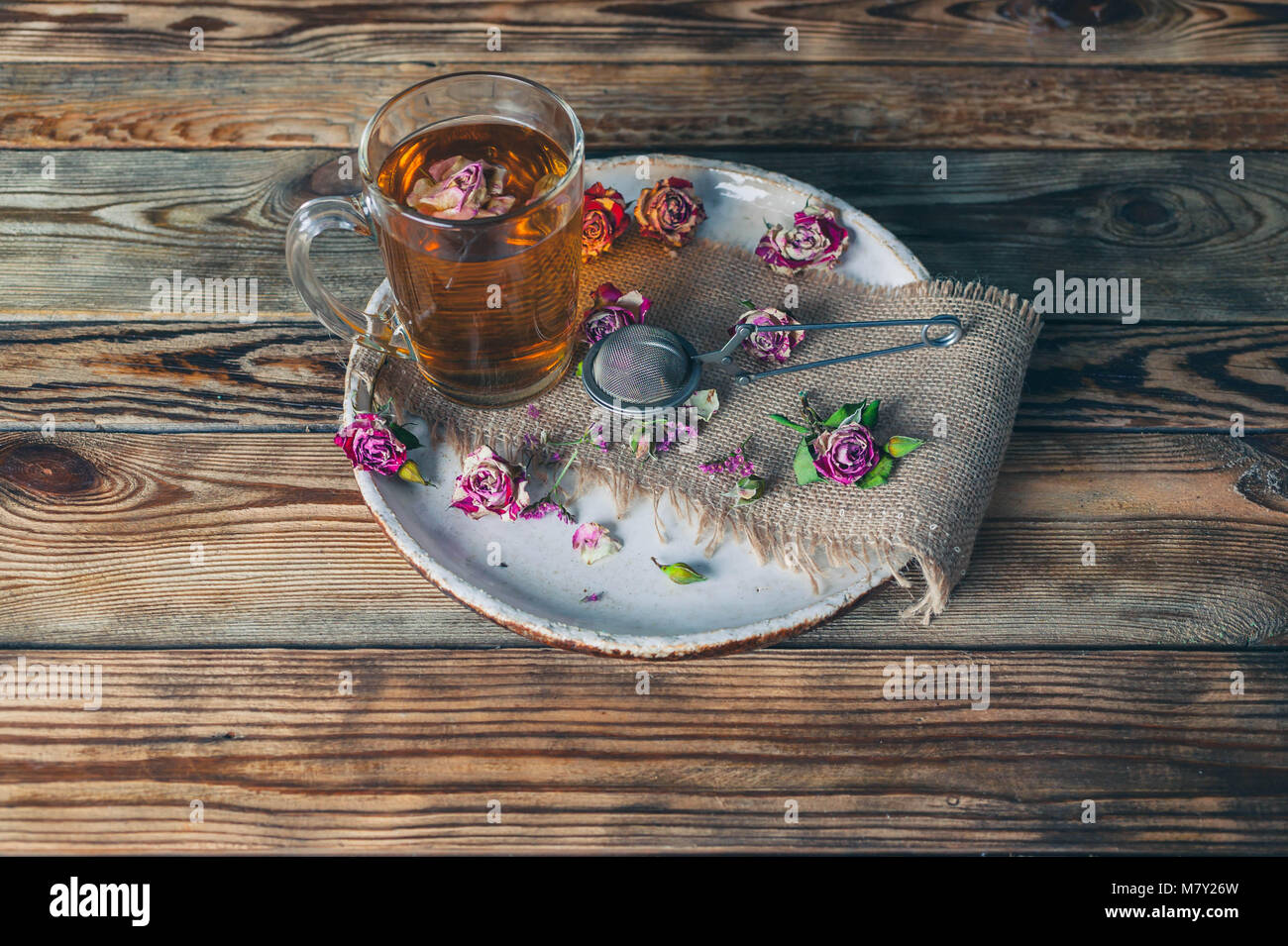 Rose buds tea, tea cup, strainer and glass jar with rosebuds. Selective focus. Stock Photo