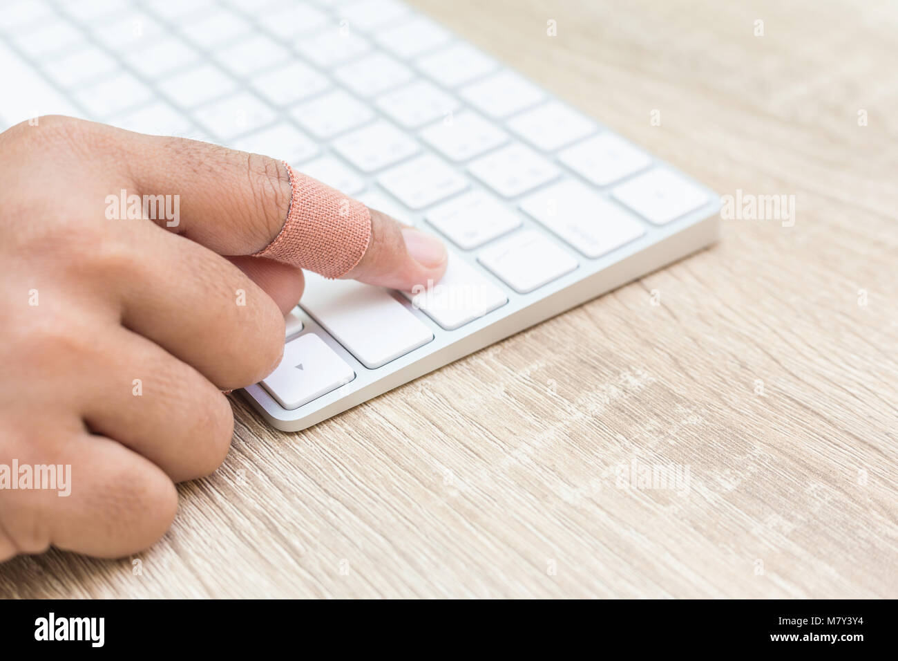 Close up hand with injury on finger using white computer keyboard on wooden background Stock Photo