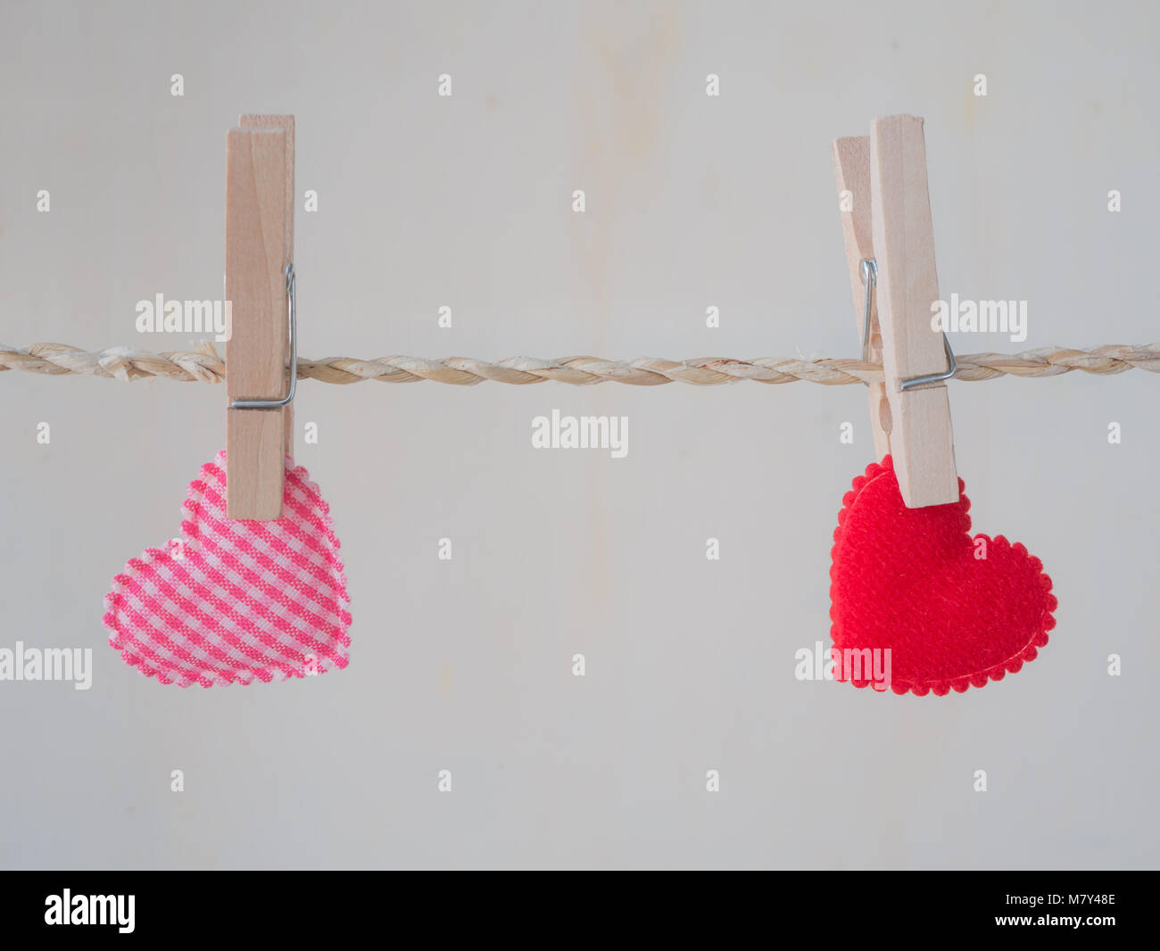 Pink heart pattern and red heart attached to a clothesline with pin on white background, Stock Photo