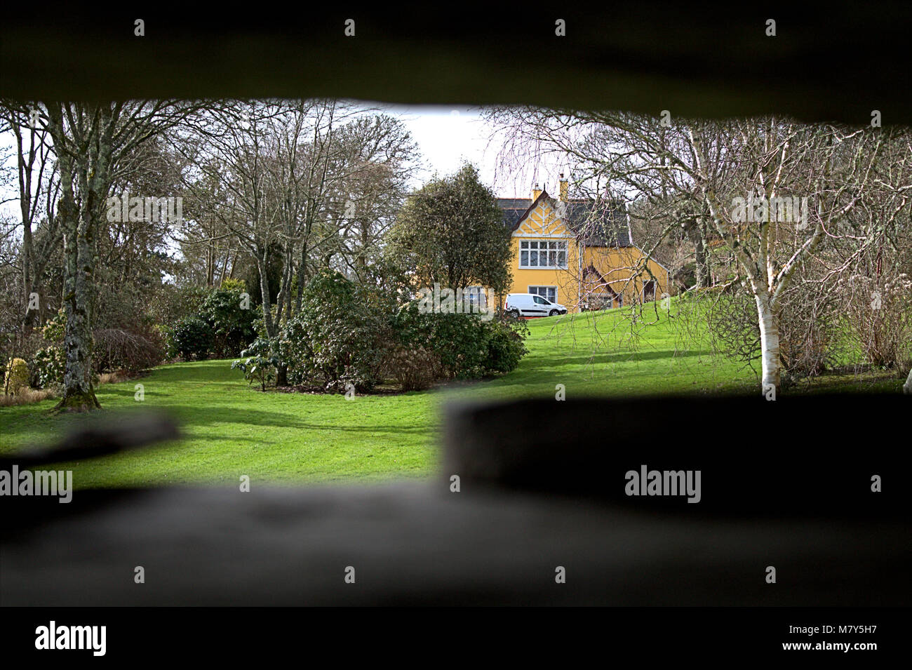 View through hole of house and gardens in the distance through a hole in the wall. Stock Photo