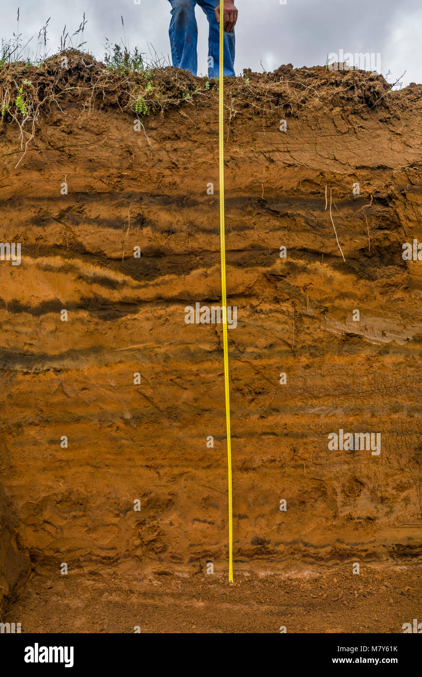 Meauring the multiple layers of earth showing deposits of ash from eruptions and volcanic activity, South Coast, Iceland Stock Photo