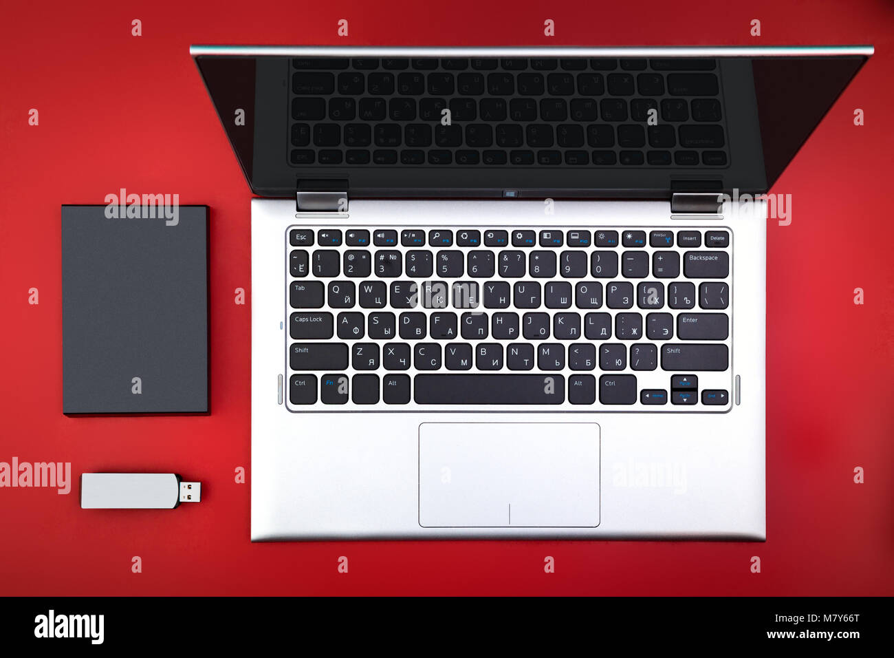 A flash drive, an external hard drive and an open laptop on a red desk