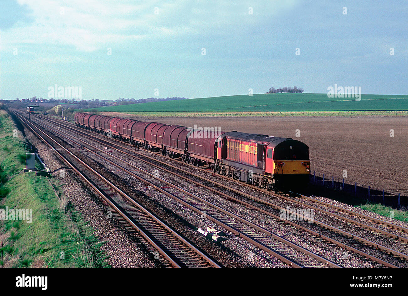 A class 58 diesel locomotive number 58033 working a train of empty steel carrying wagons approaching Manor Farm bridge near Cholsey on the 26th March 2002. Stock Photo