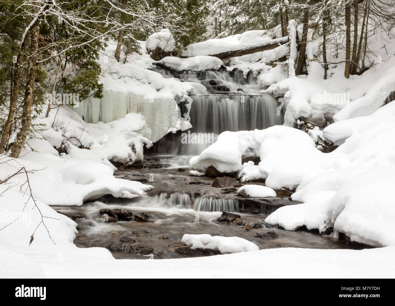 Waterfall in Winter. Wagner Falls in Munising Michigan, surrounded by freshly fallen snow. Snow lines tree branches and lacy ice patterns, frame the w Stock Photo