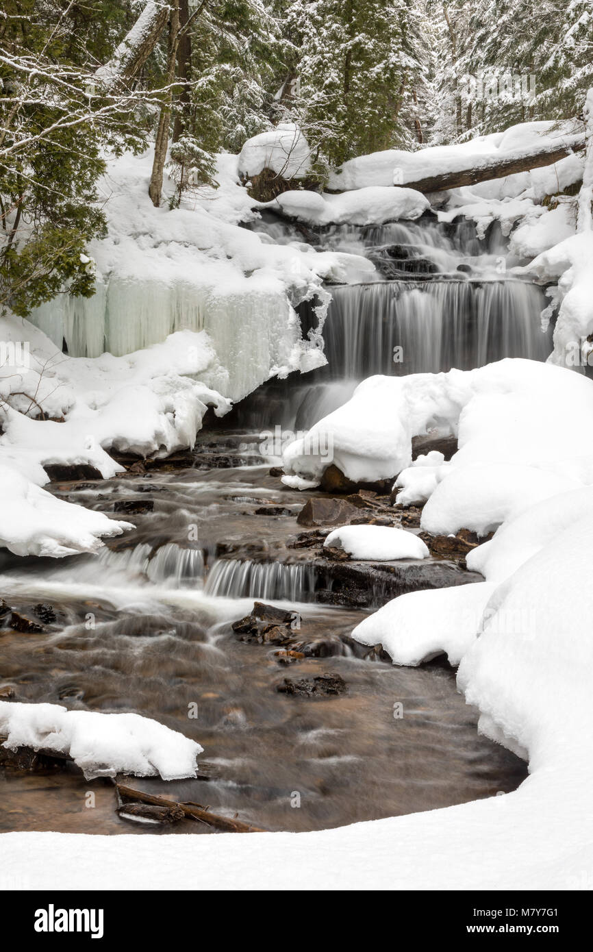 Waterfall in Winter. Wagner Falls in Munising Michigan, surrounded by freshly fallen snow. Snow lines tree branches and lacy ice patterns, frame the w Stock Photo