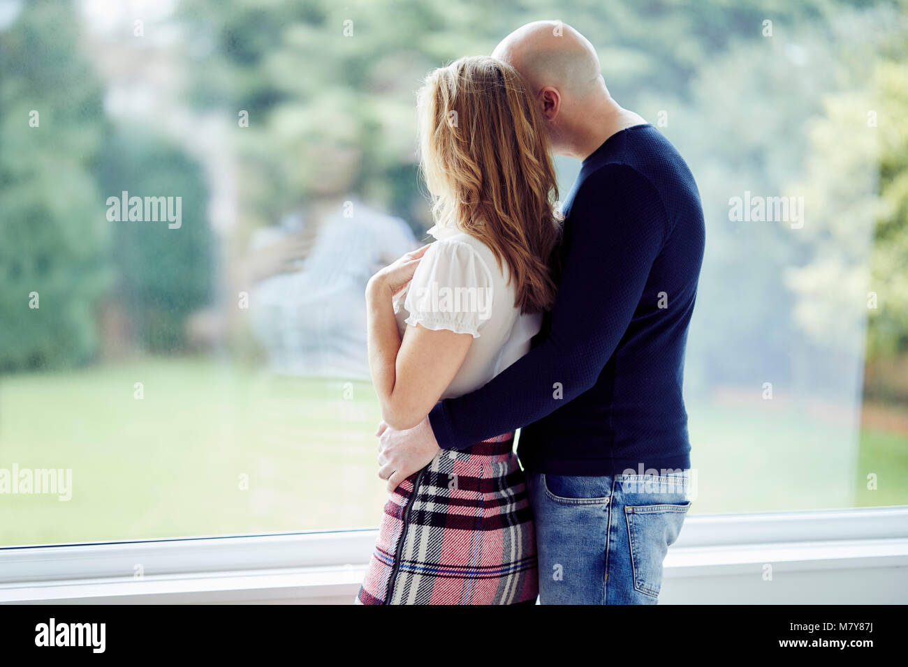 Couple stood looking out of window Stock Photo