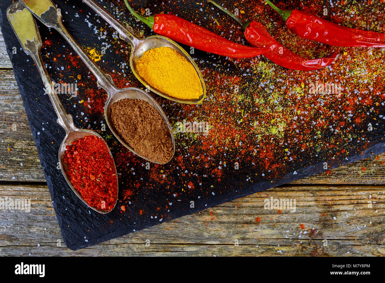 Overhead view depicting cooking with spices in a rustic kitchen with bowls of colourful ground spice and scattered powder on an old scored wooden coun Stock Photo