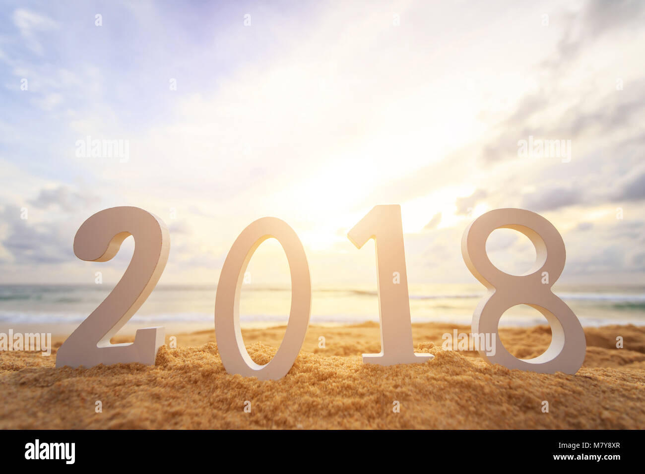 New year concept : Close up white wooden alphabet 2018 setup on the sunset beach. Warm tone color with lens flare. Stock Photo