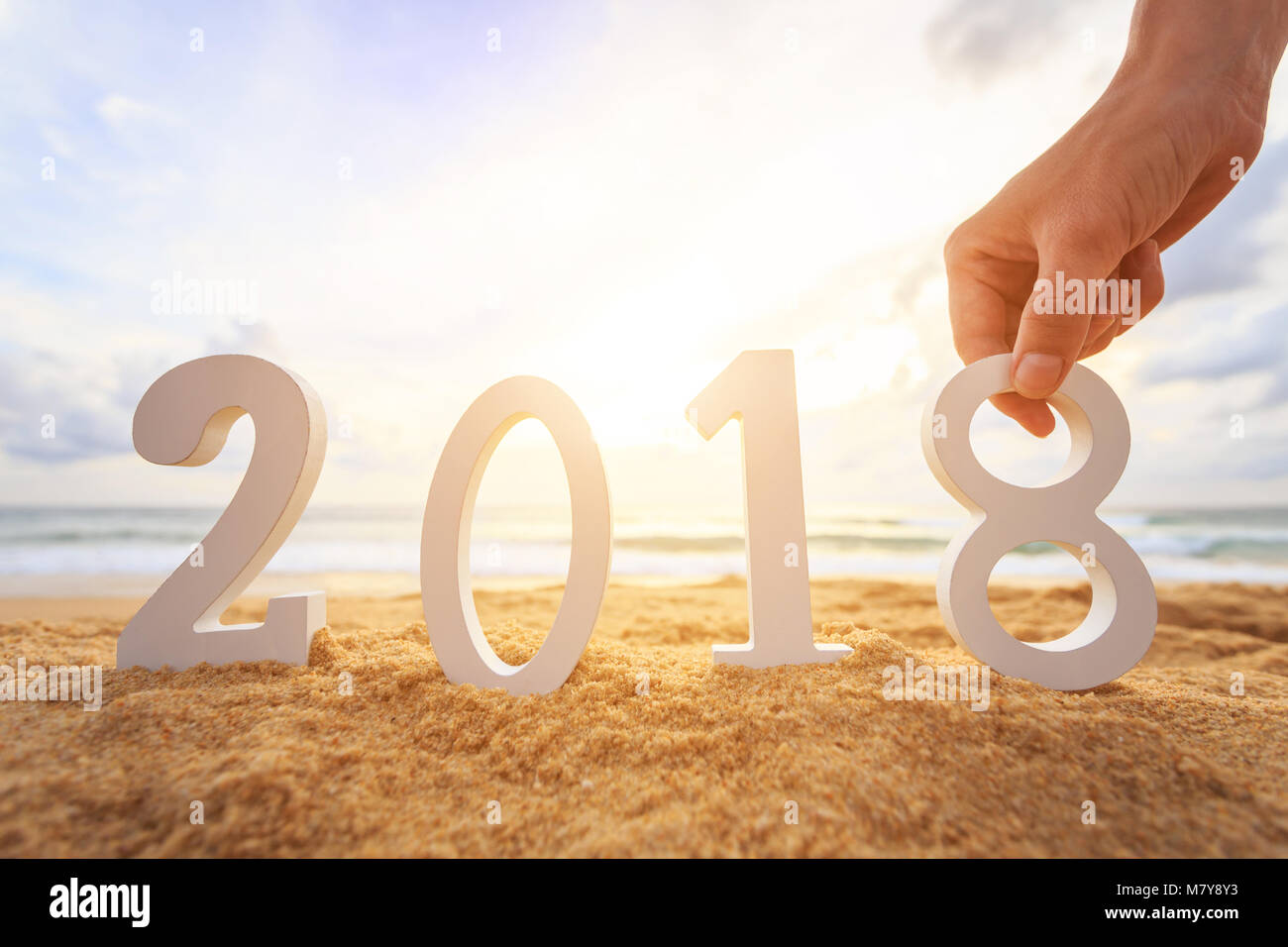 New year concept : Close up hand holding and set up white wooden alphabet 2018 on the sunset beach. Warm tone color with lens flare. Stock Photo