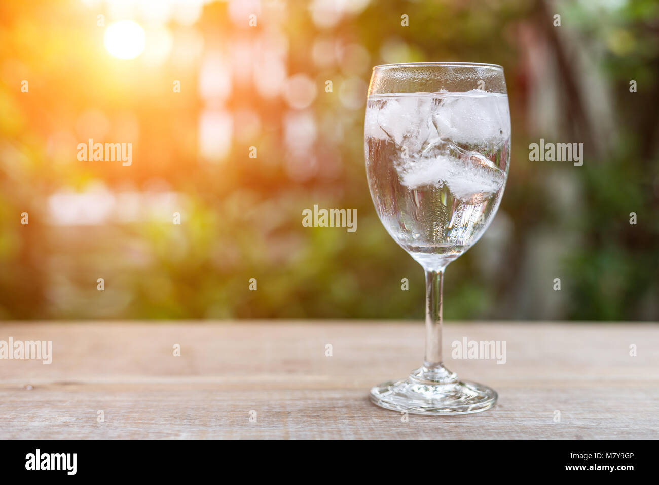 Close up glass of cold water with ice on table with blur nature garden background Stock Photo