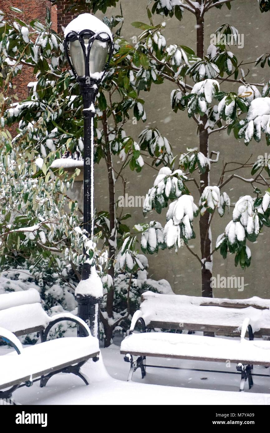 An old-fashioned street lamp, plants, and benches covered in snow in a ...