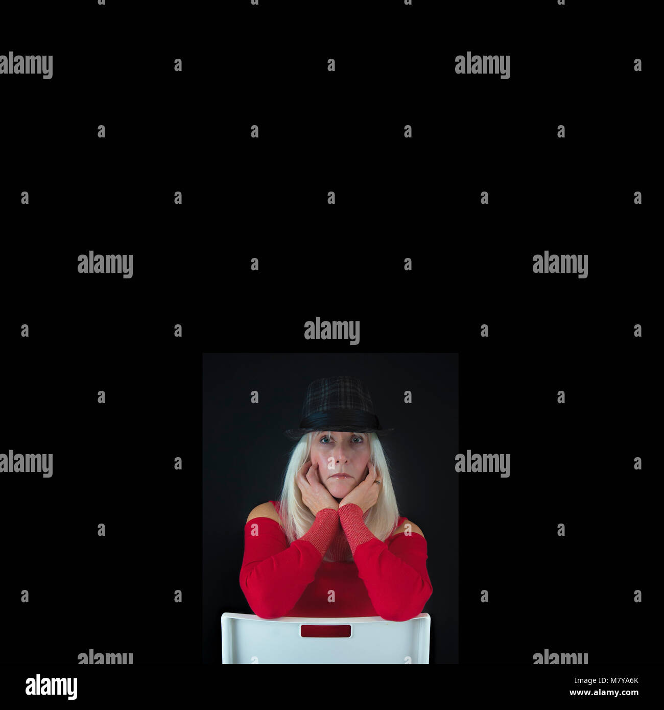Minimalist Portrait with copyspace. of a mature woman with long white hair dressed in red sweater wearing a gray and black hat sitting on a backward wh Stock Photo