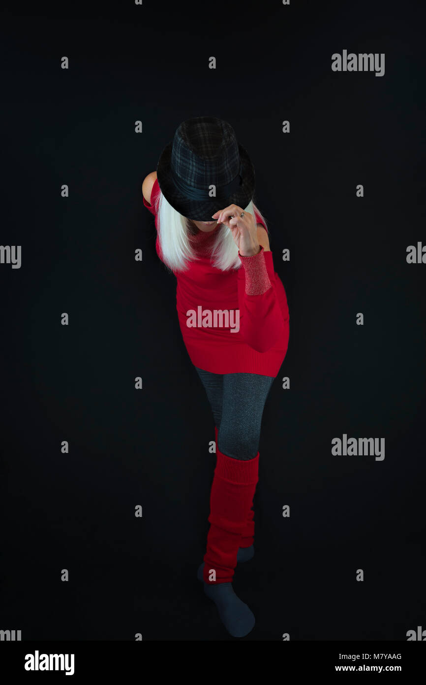 A mature woman wearing gray leggings and socks, red sweater and leg warmers and a black and gray hat on top of a head of white hair, taking a bow in t Stock Photo