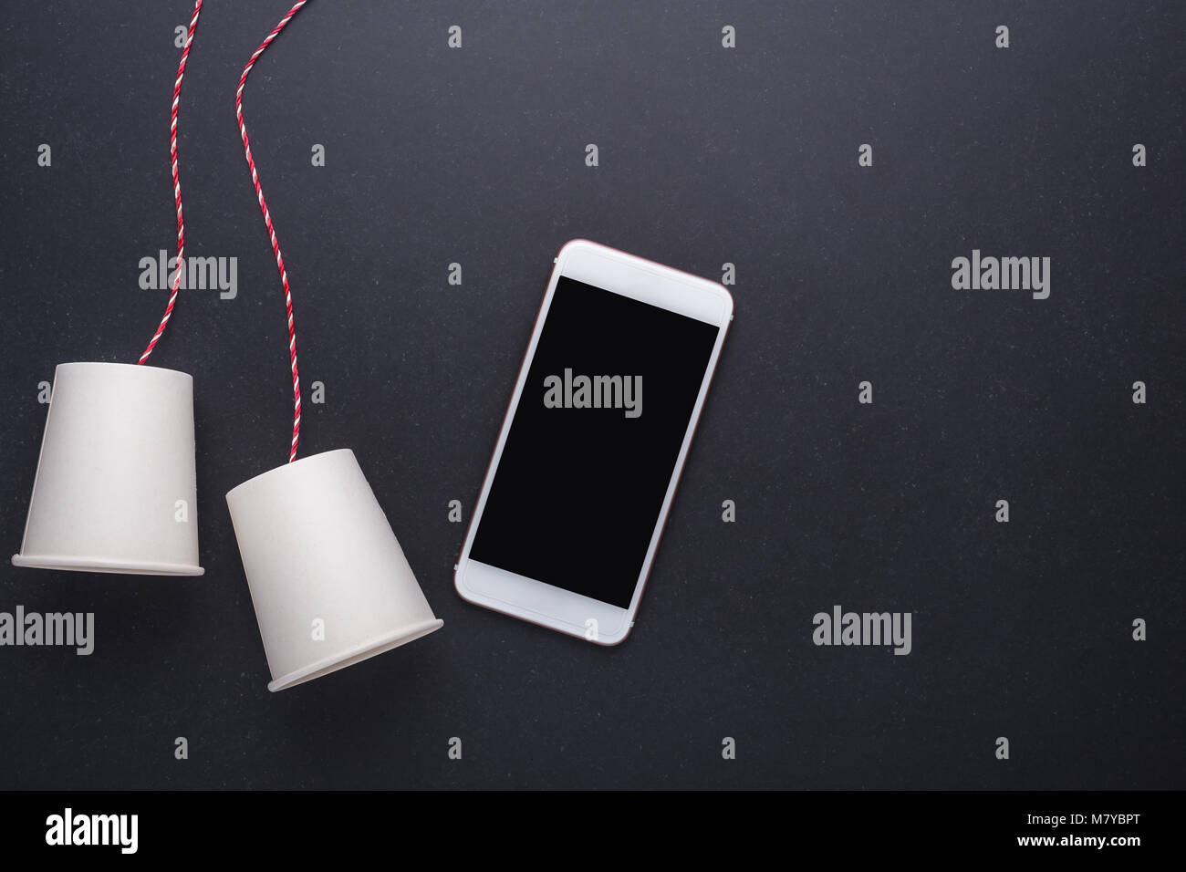 Two white paper cup connect with red rope used for classic phone and modern smartphone on black stone table board background. For compare the old and Stock Photo