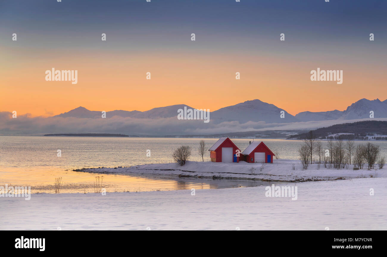 A Winter landscape in northern Norway with snow, mountains, fjords and a red cottage at Sunset. Stock Photo