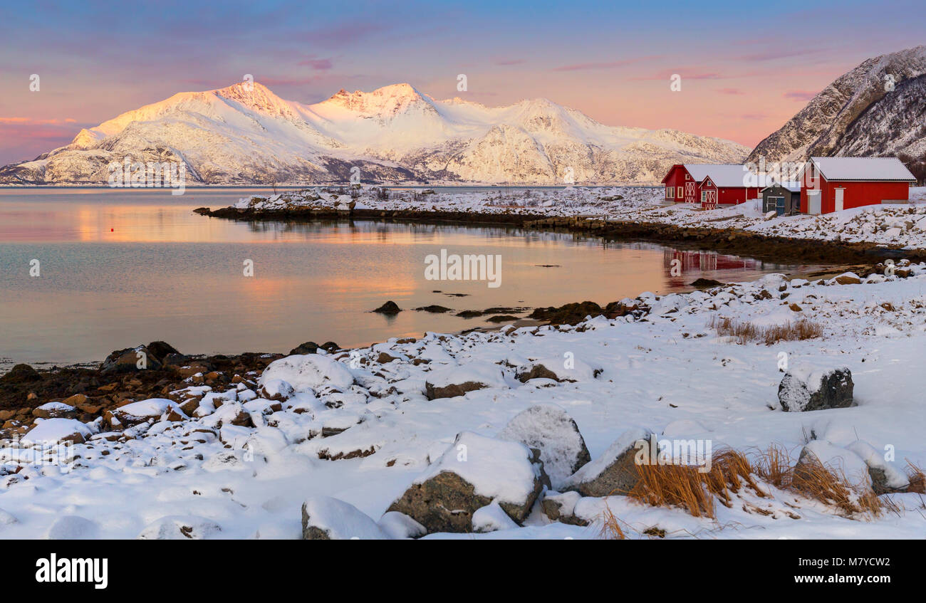 Winter landscape image of snow covered coastal scenery in Northern Norway with red cottages along the waterfront. Stock Photo