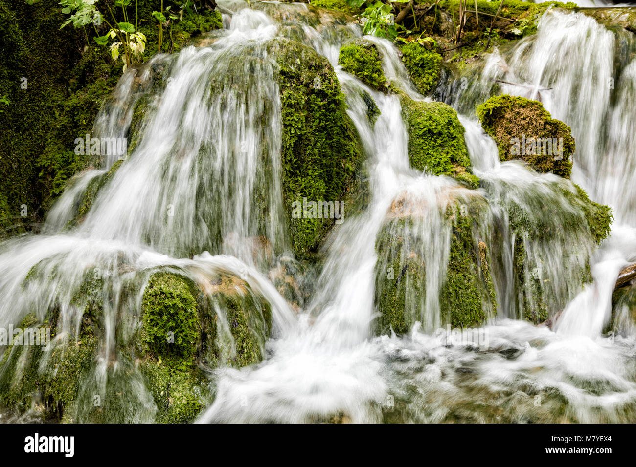 Close-up of a small waterfall cascading over moss-covered travertine at Plitvice Lakes National Park.