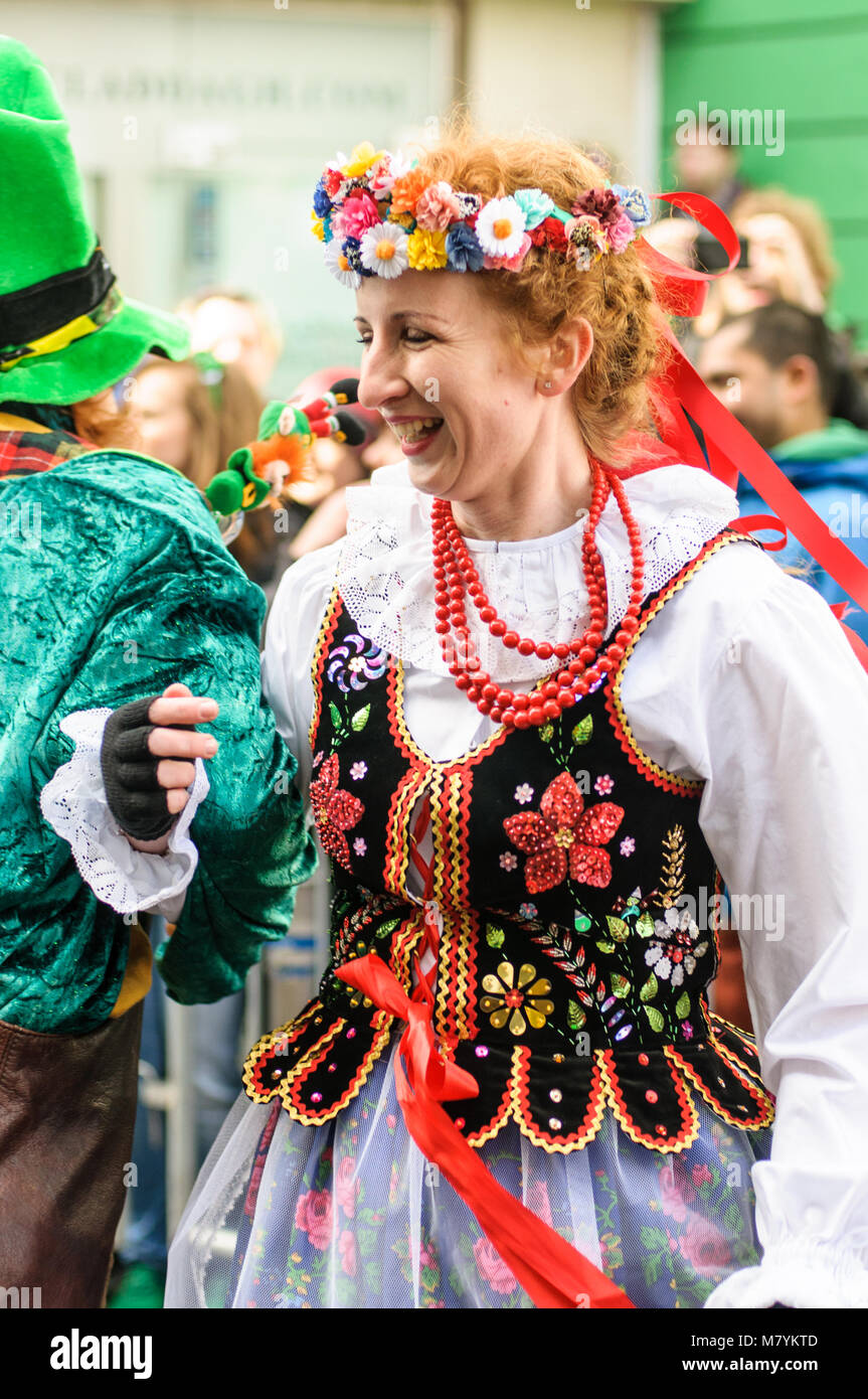 Polish woman in traditional dress is dancing with leprechaun  during the St Patrick's Day parade in Galway, Ireland. Stock Photo