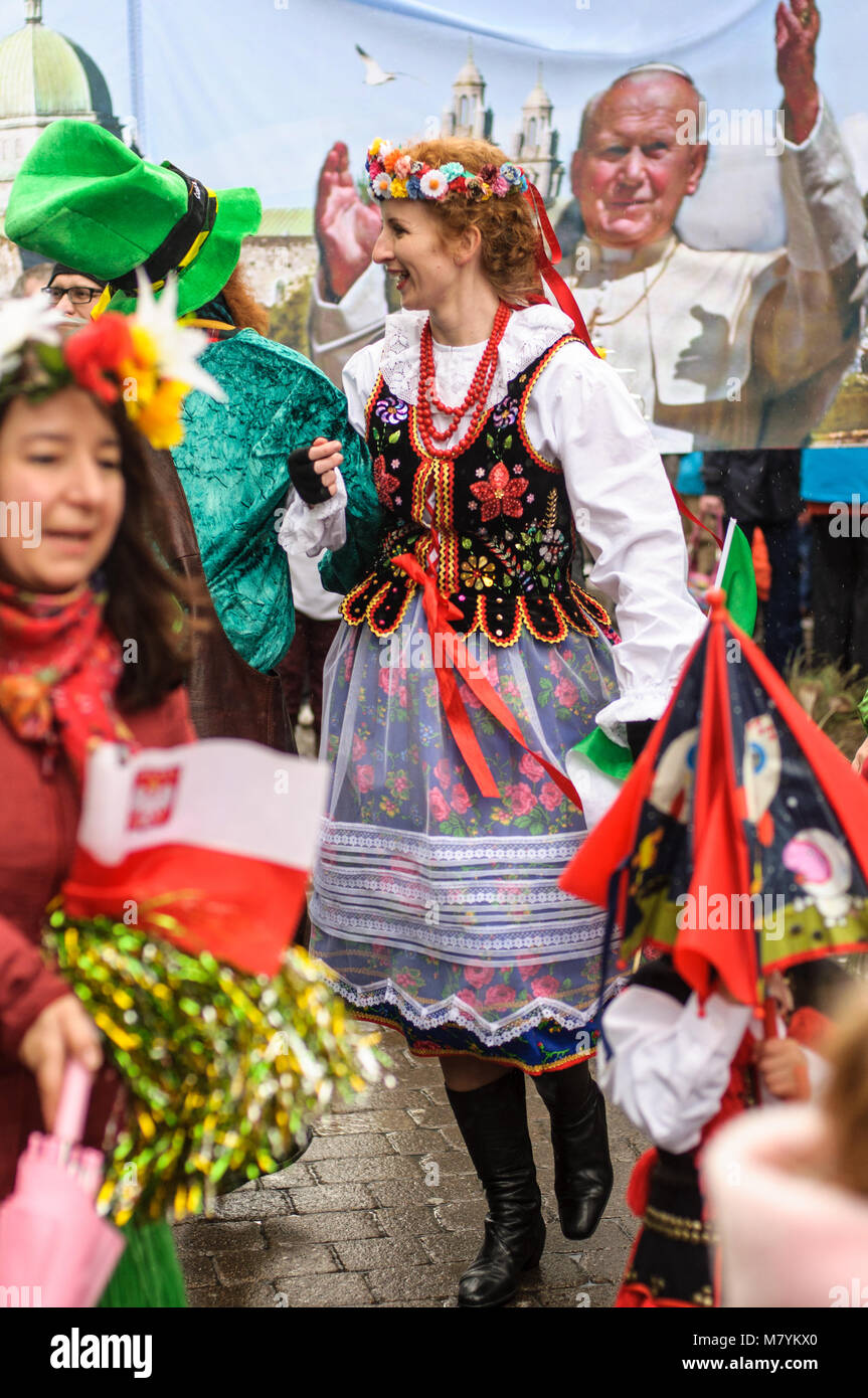 Polish woman in traditional dress is dancing with leprechaun  during the St Patrick's Day parade in Galway, Ireland. Stock Photo