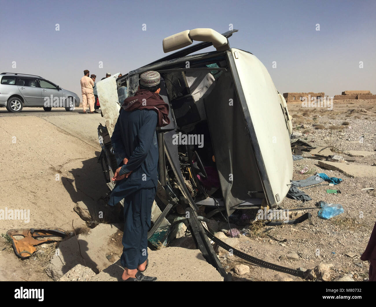 Kandahar, Afghanistan. 14th Mar, 2018. A man stands in front of the damaged passenger bus at a road accident site in Kandahar province, Afghanistan, March 14, 2018. At least seven passengers lost their lives and 24 others were injured in a road accident in Kandahar province, south of Afghanistan on Wednesday, a local official said. Credit: STR/Xinhua/Alamy Live News Stock Photo