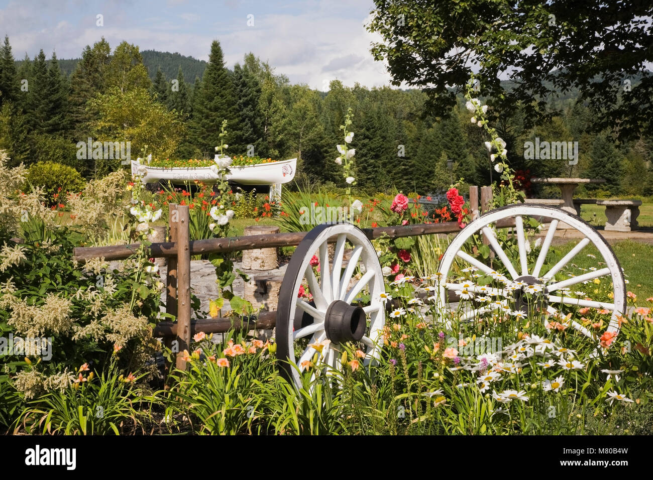 Wagon wheels and flowers in a garden border in a landscaped residential backyard garden in summer. Stock Photo