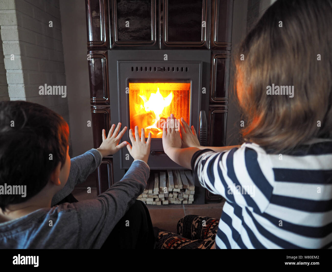 little girl and little boy warm up by the fireplace Stock Photo