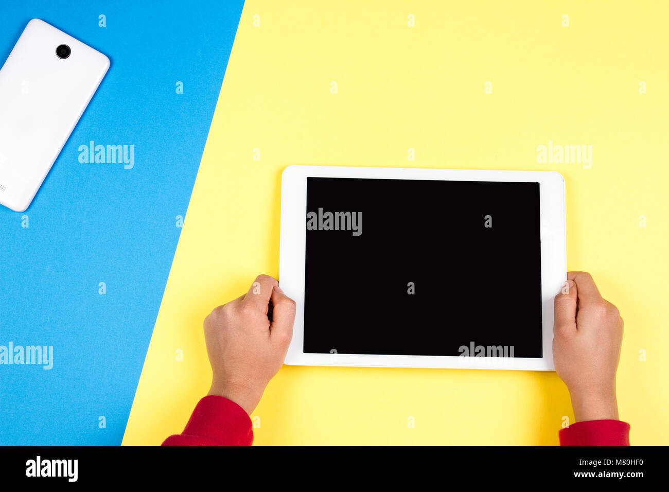 Kid hands holding tablet computer on blue and yellow background Stock Photo