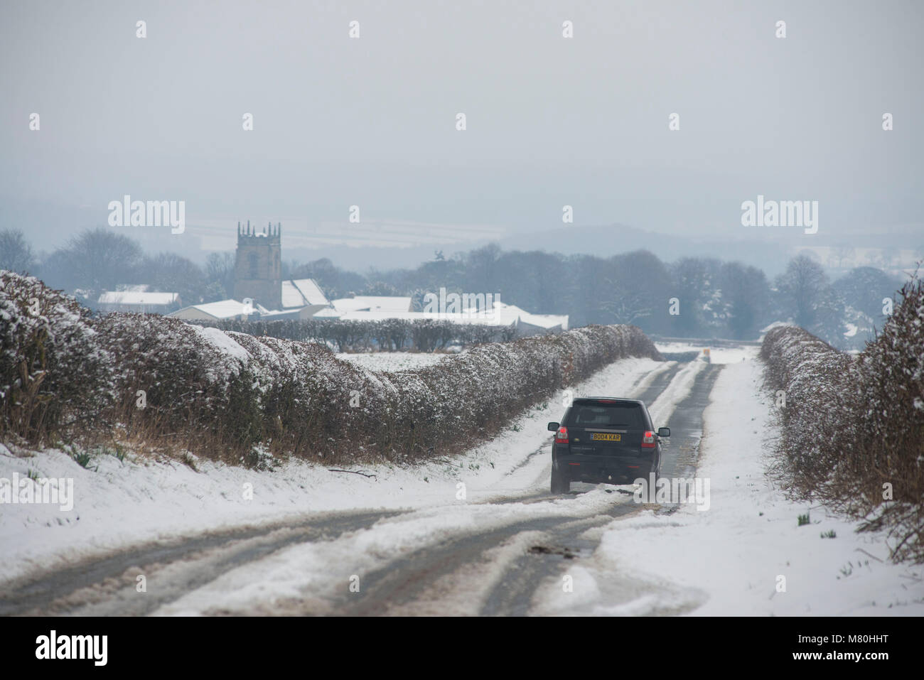 A 4x4 vehicle travels down a snow covered road at Woolley, West Yorkshire, UK. Stock Photo