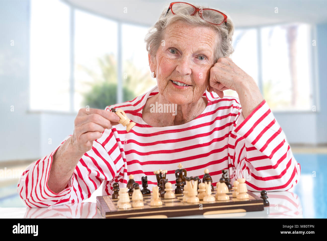 Senior old woman playing chess, moving pieces across the chessboard on large glass background Stock Photo