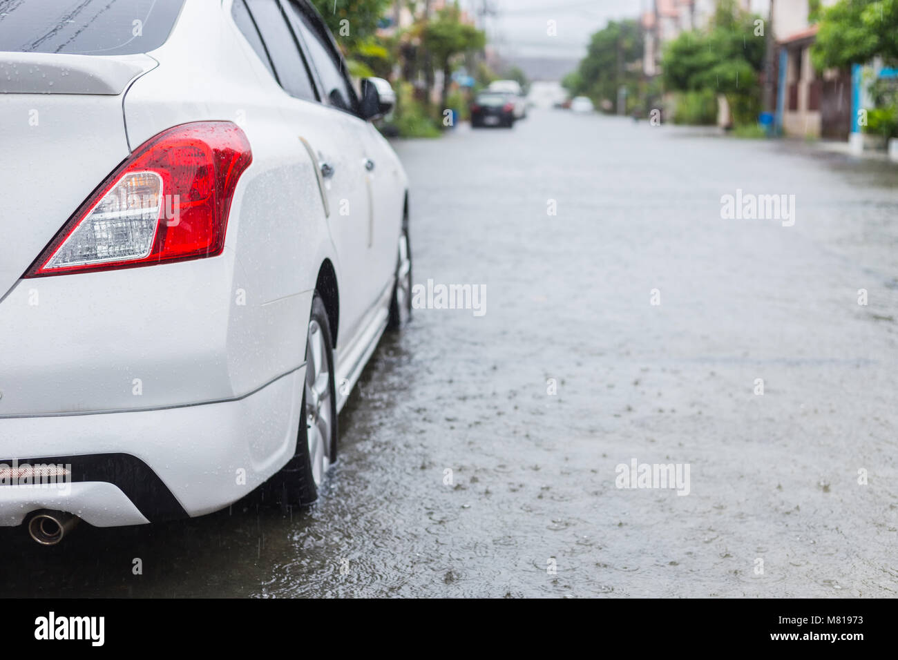 Car parking on the street of village while raining and show level of water flooding in Phuket, Thailand Stock Photo