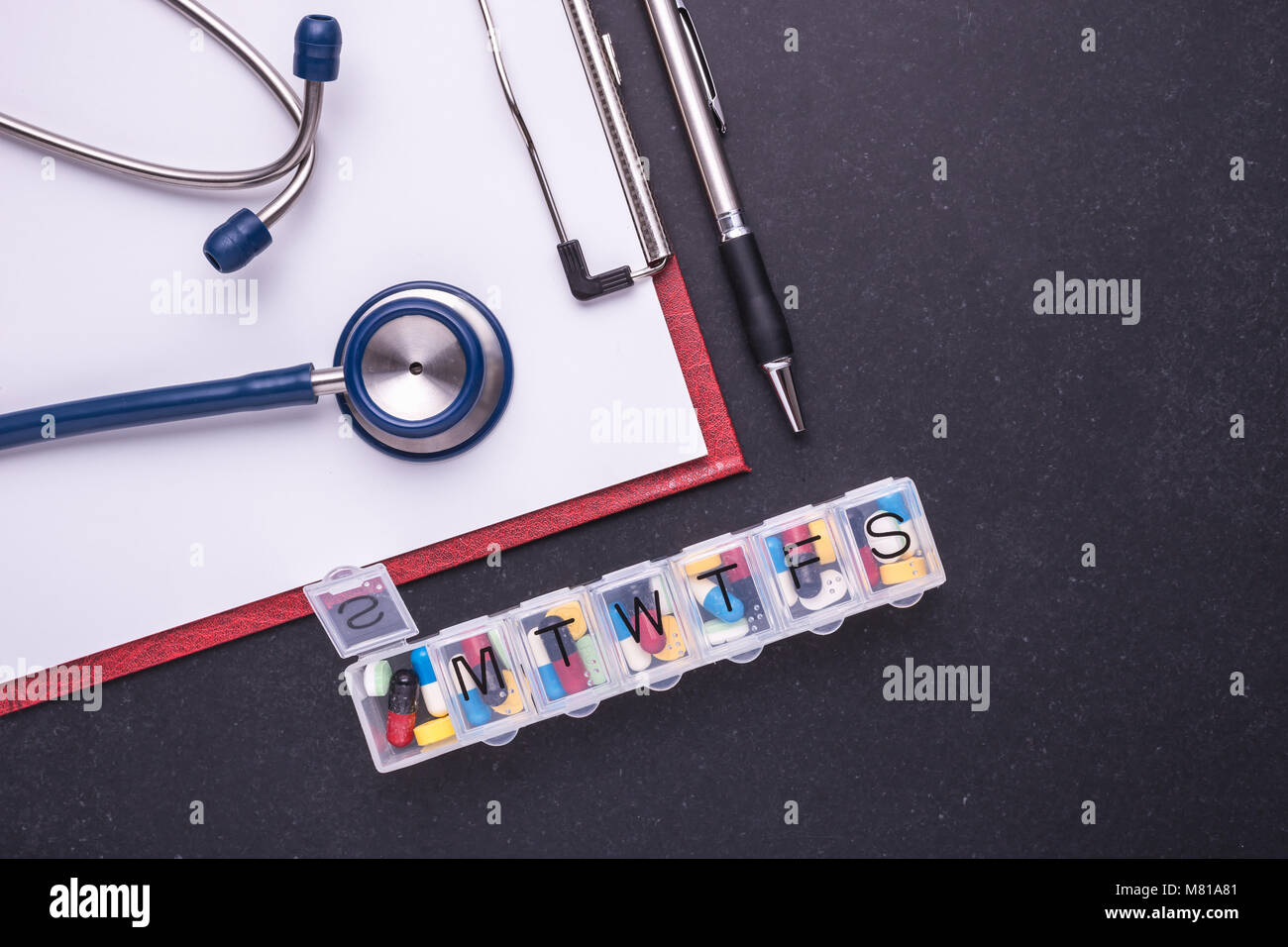 7 day plastic pill organizer, doctor stethoscope on dark table background. Health care concept. Top view Stock Photo