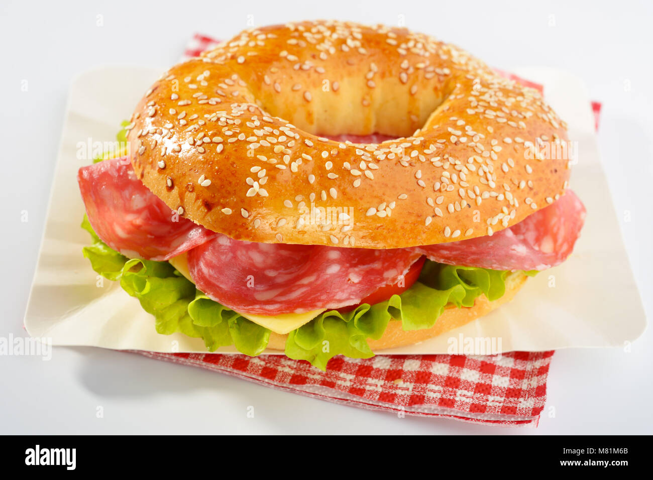 Bagel sandwich with sausage, cheese, and lettuce on a paper plate Stock Photo