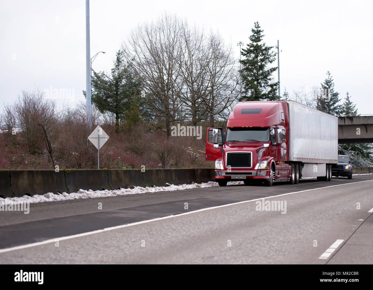Road patrol police officer checks stopped long-haul red modern big rig semi truck with reefer semi trailer on winter straight interstate multiline hig Stock Photo