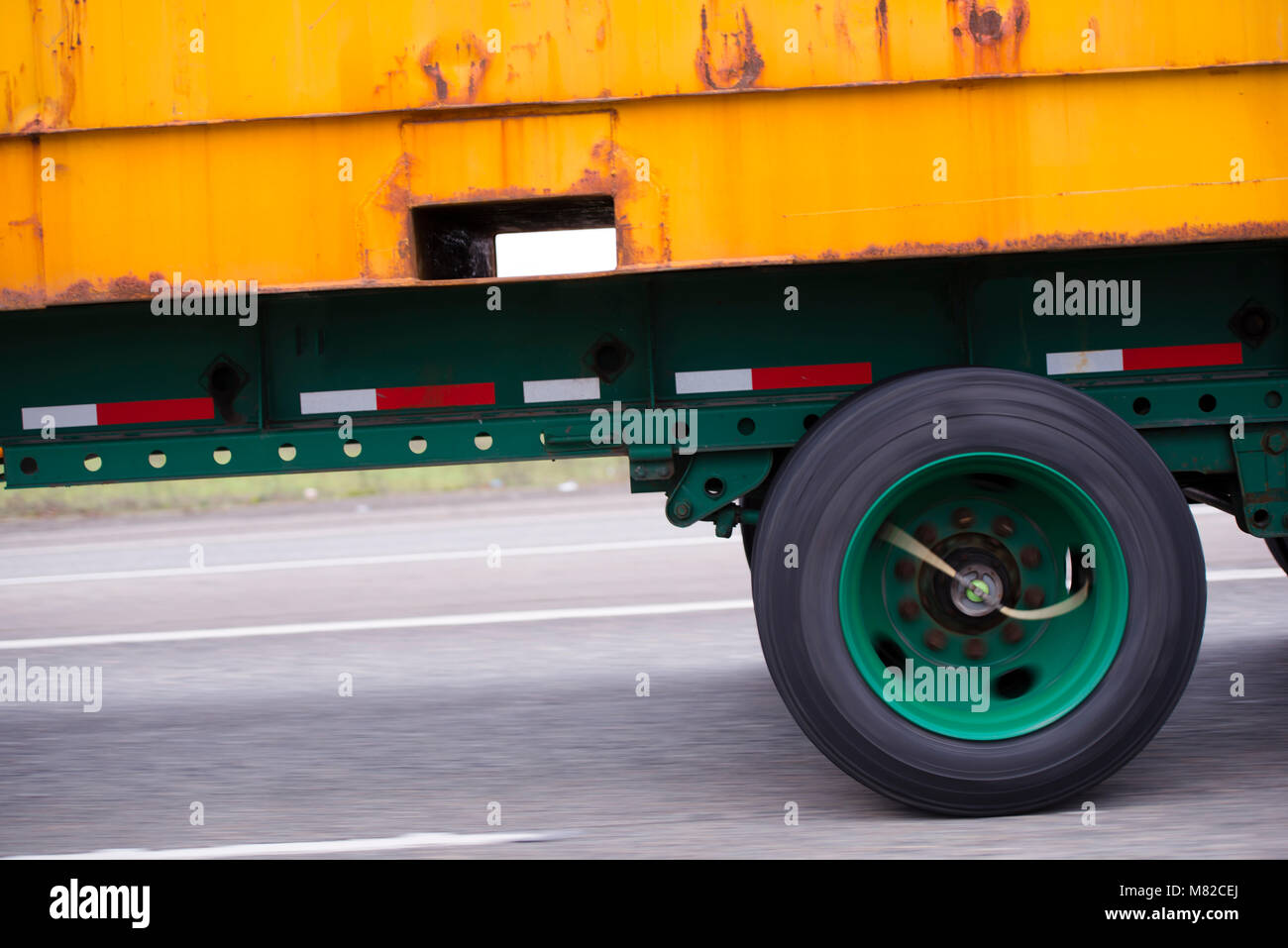 Yellow rusty container on flat bed semi trailer with green wheels on green trailer frame driving on the multiline road Stock Photo