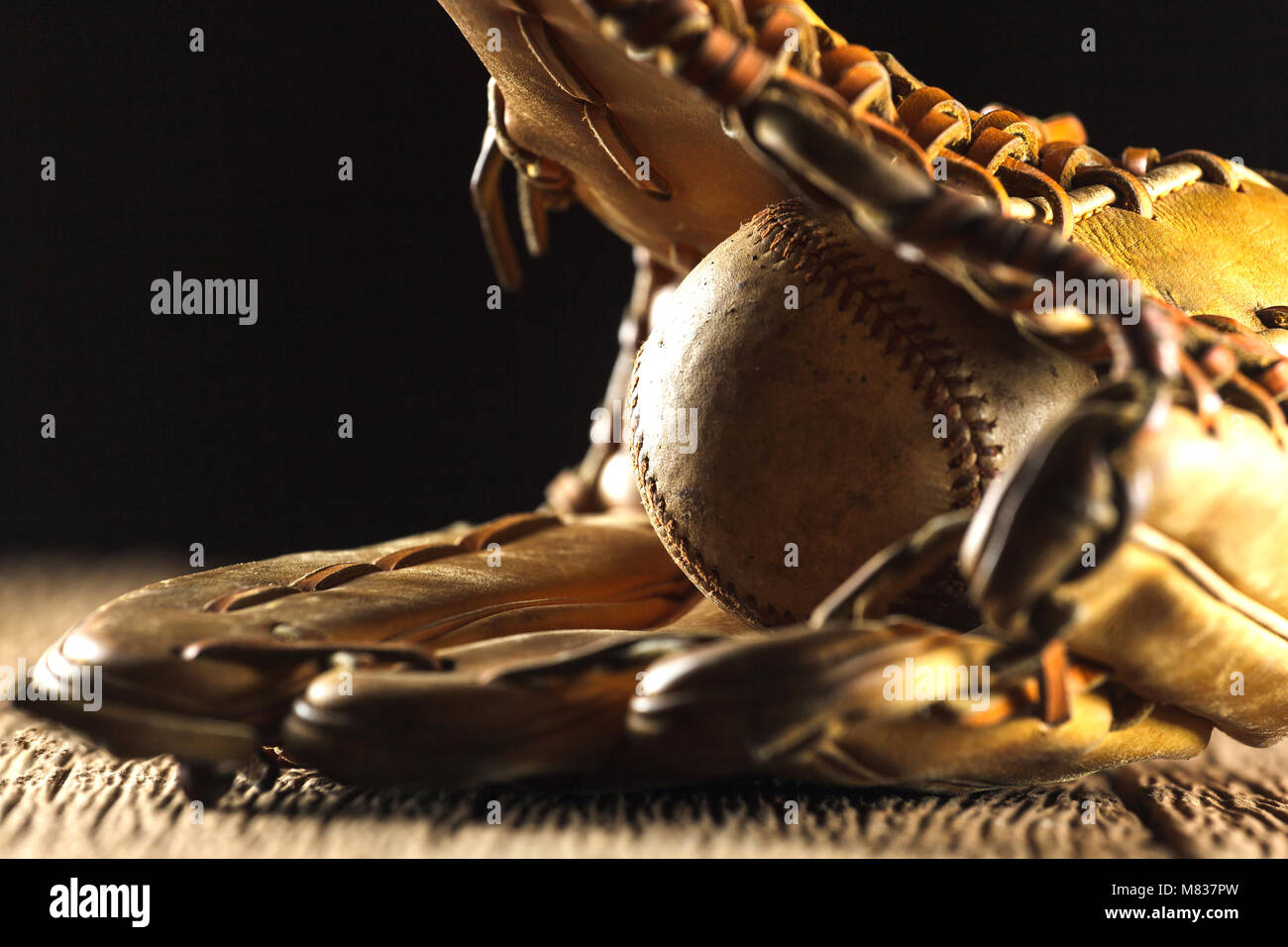 Close up image of an old used baseball and baseball glove on wooden