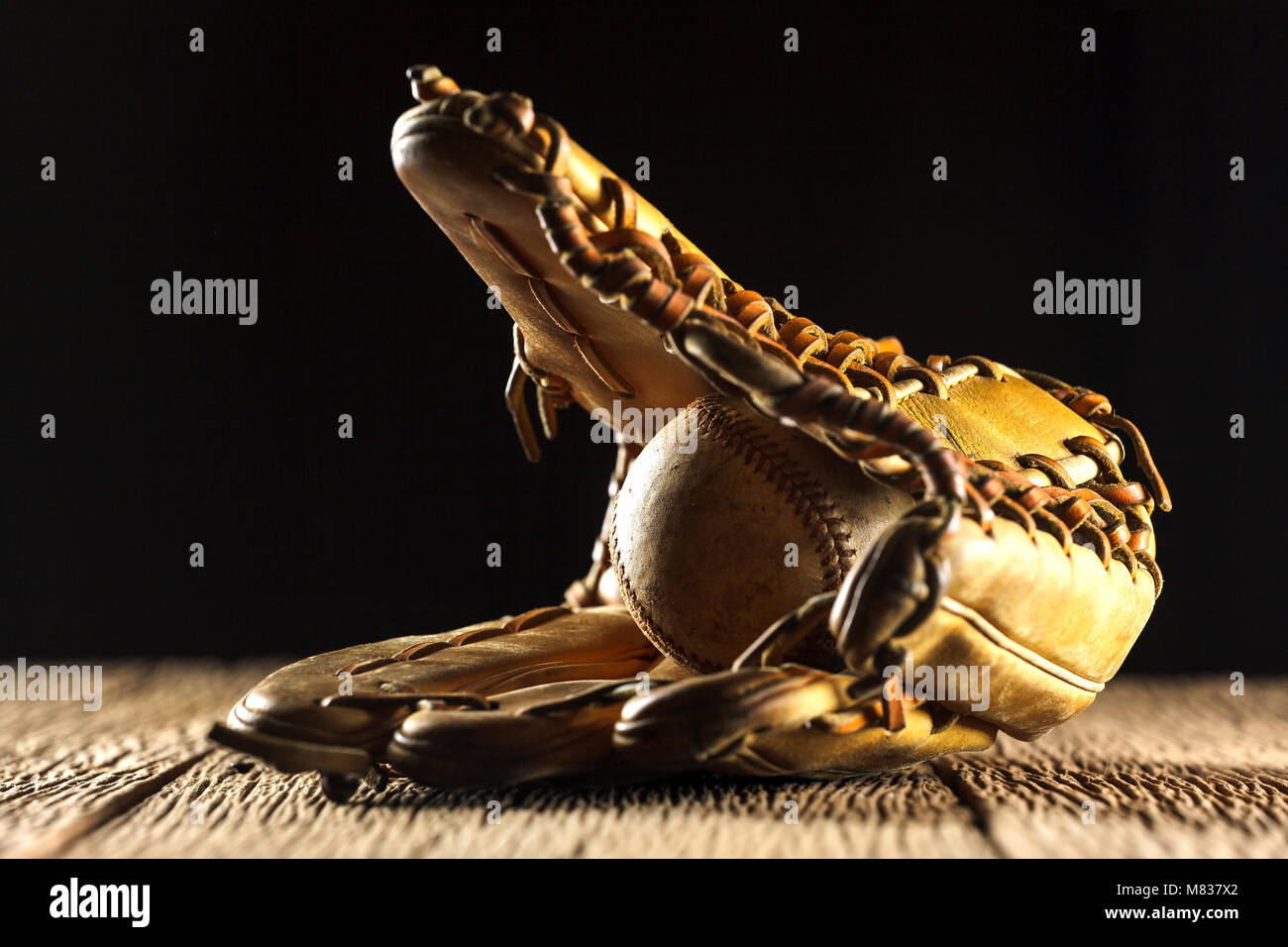 Close up image of an old used baseball and baseball glove on wooden
