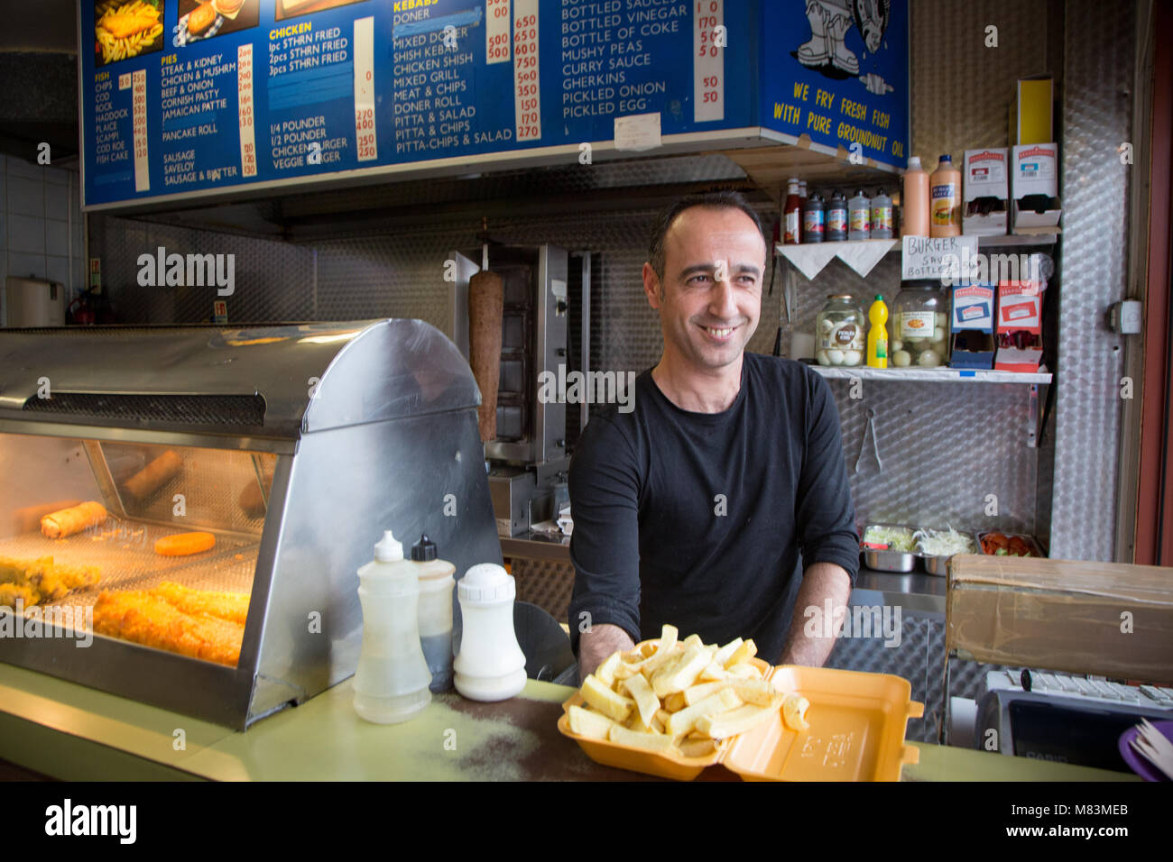 Man serving chips at a takeaway fish and chips restaurant Stock Photo
