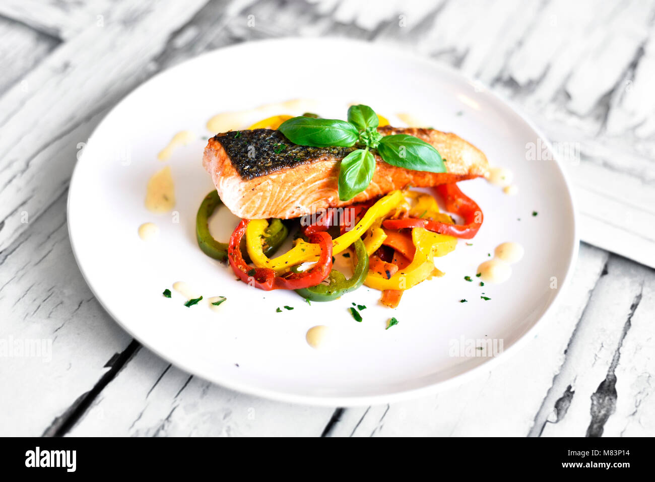 Delicious salmon filet and red bell pepper vegetables on a white plate. Healthy meal, decorated with basil leaf. Grilled salmon filet. Stock Photo