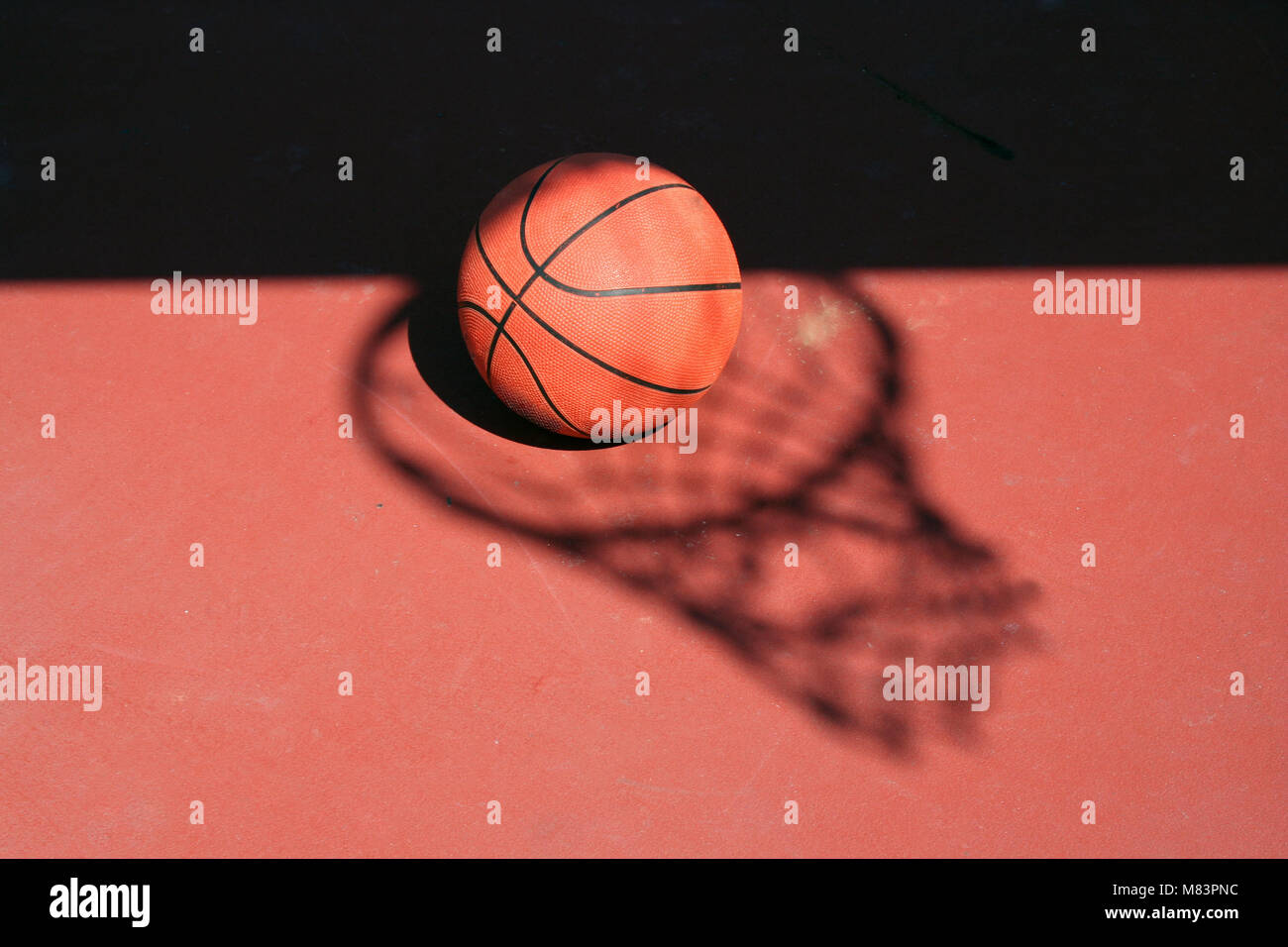 A Basketball and net shadow on a red court Stock Photo