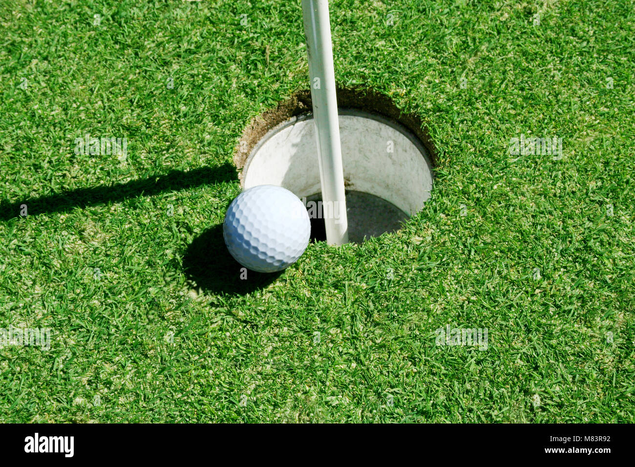 A Golf Ball on green near hole with flag pole Stock Photo